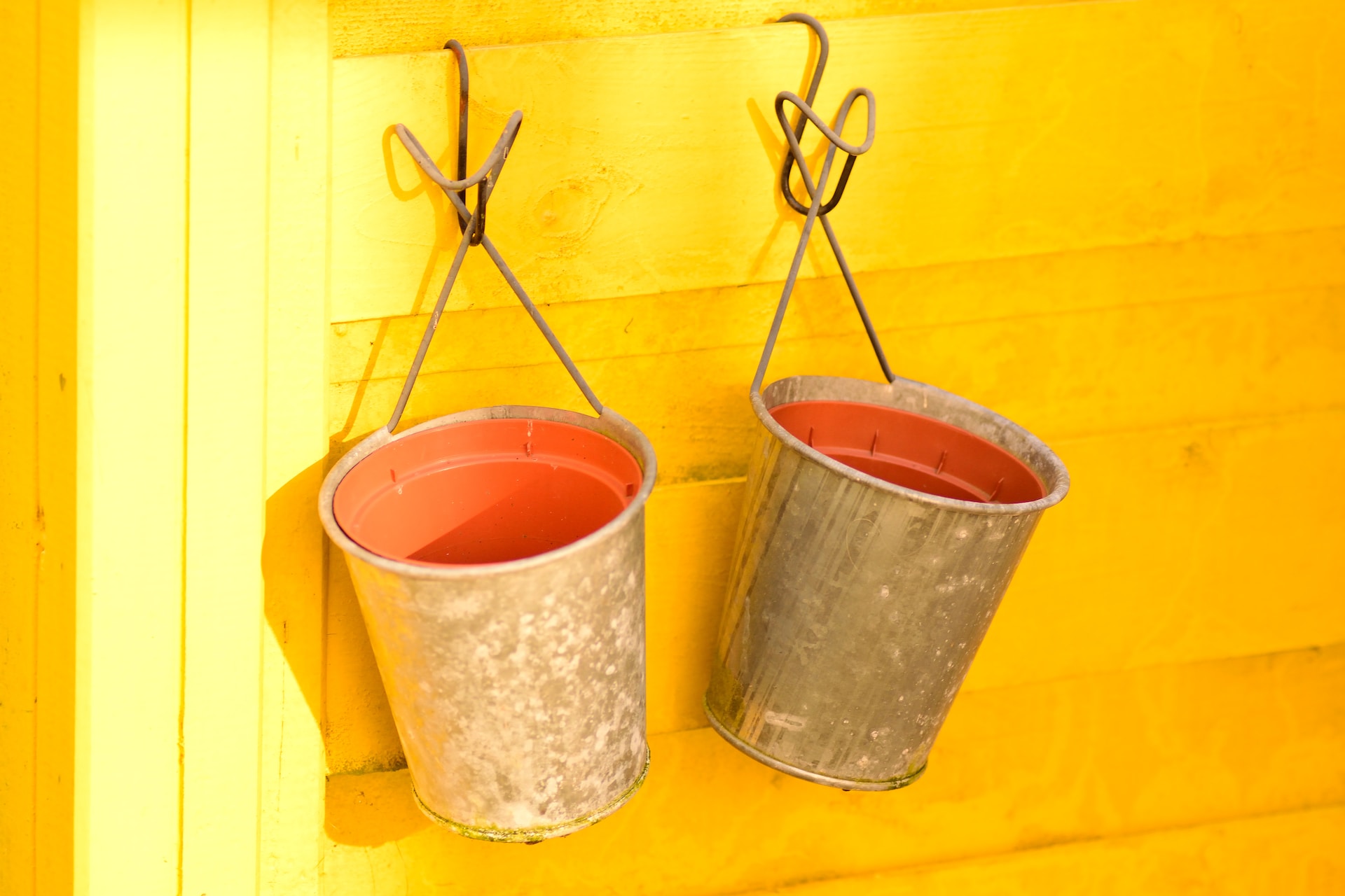 Two metal buckets hanging from hooks on a bright yellow wall